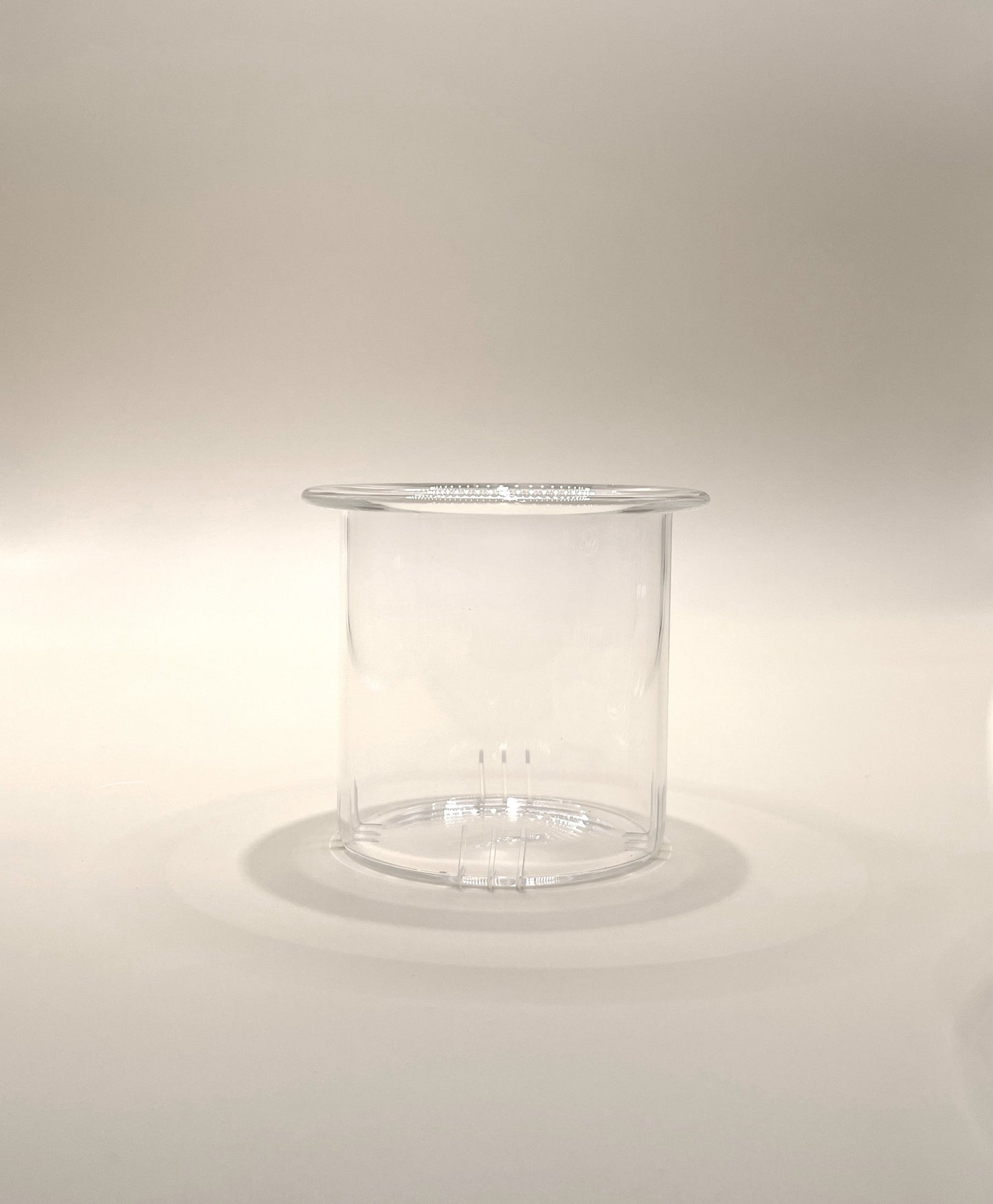 A transparent, cylindrical plastic container with a slightly flared top edge. Reminiscent of the My Store Crystal Clarity Teapot with its pristine appearance, the 600ml container is empty and placed on a neutral, light-colored surface with soft lighting creating subtle shadows.
