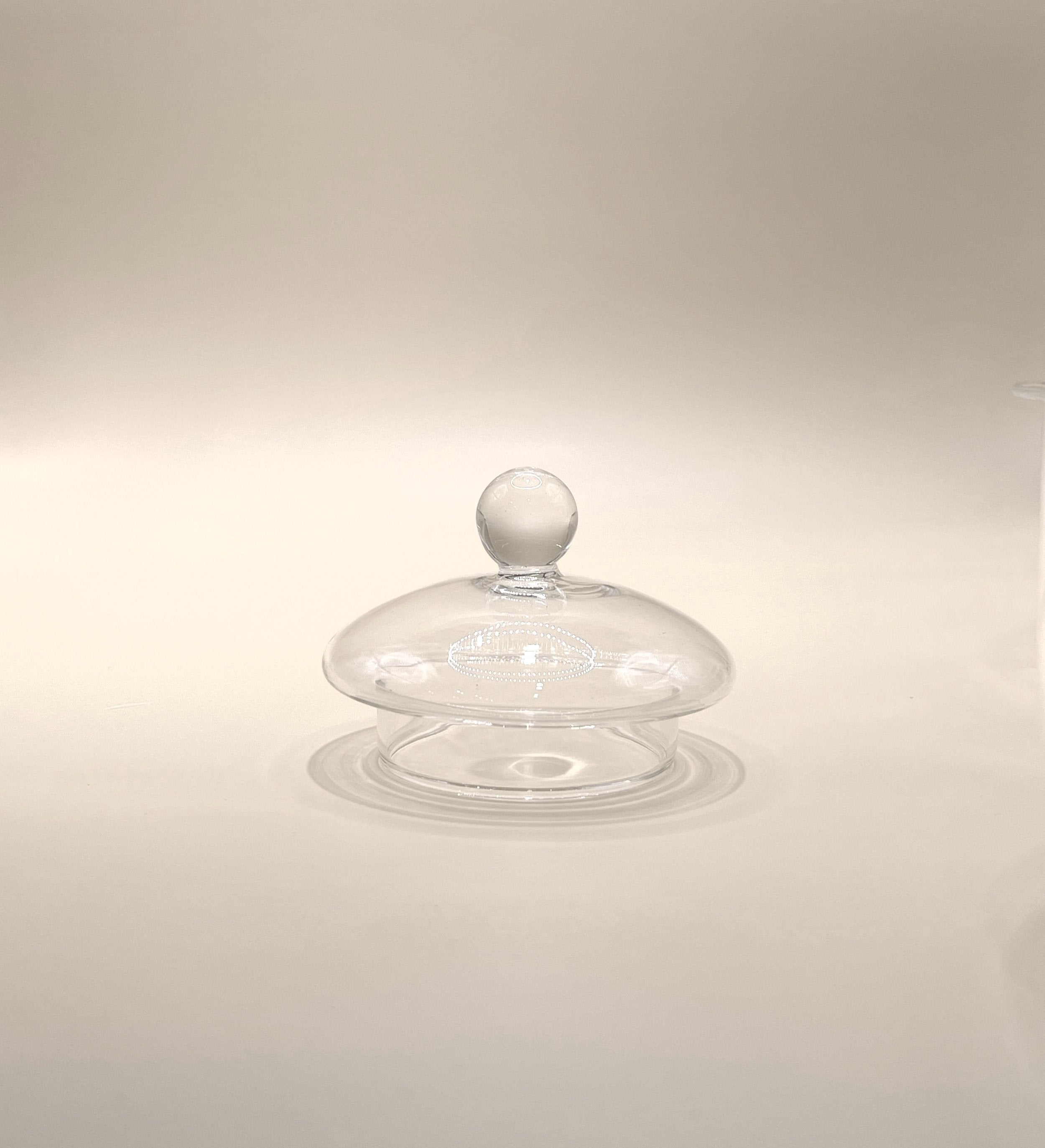A clear, 600ml Crystal Clarity Teapot by My Store, featuring a round knob on top that resembles a lid or dome, is centered against a neutral background. The minimalist setup emphasizes the transparent and delicate nature of the high borosilicate glass teapot.