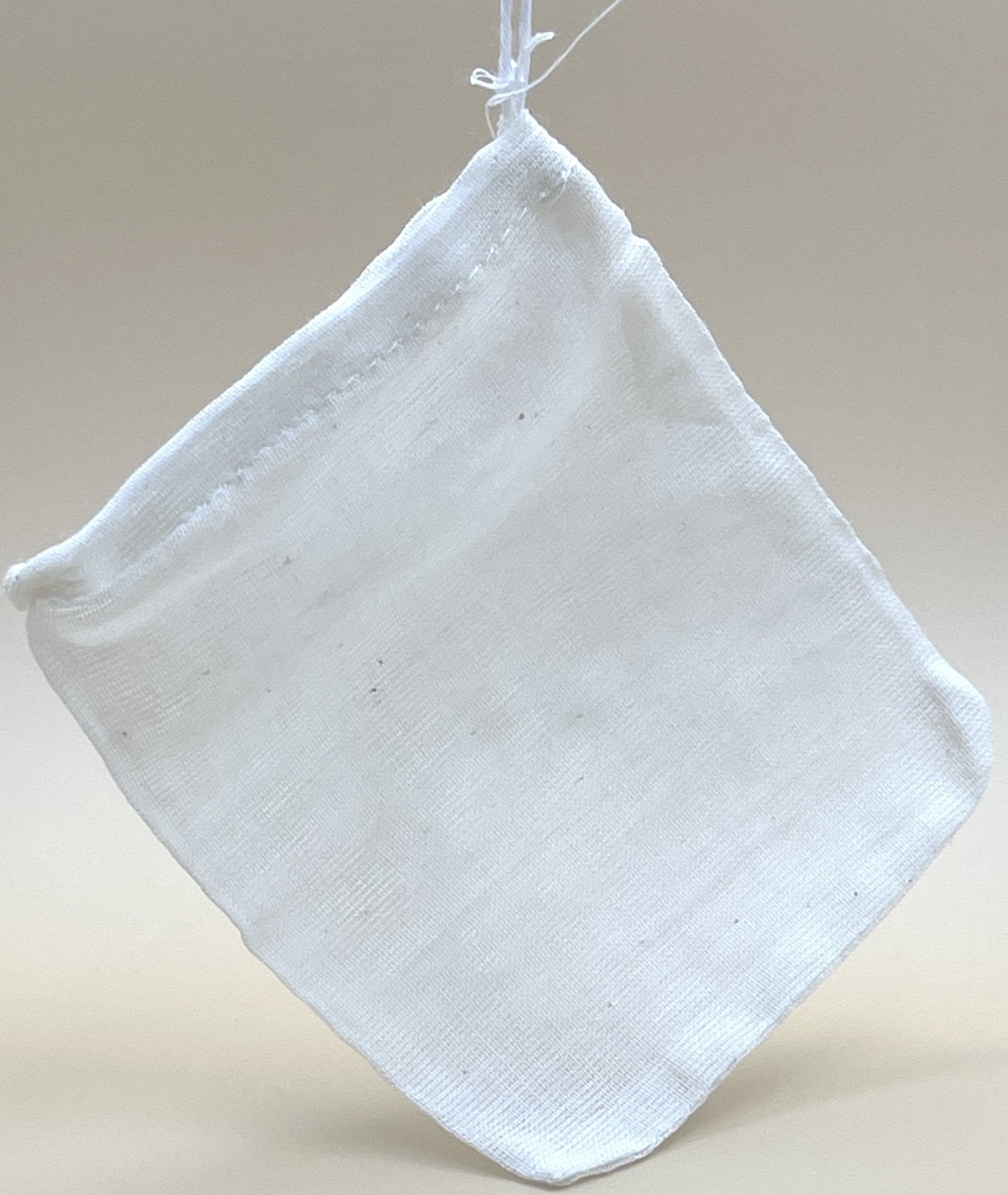 A small, white EcoPure Cotton Tea Bag from My Store hangs against a neutral background, suspended by a white string. Made from unbleached cotton, the slightly translucent bag has a drawstring closure at the top, perfect for preserving delicate flavors and aromas.