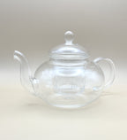 The Crystal Clarity Teapot from My Store, made of high borosilicate glass, boasts a rounded body, a curved spout, and a handle. It comes with a lid that has an elegant knob on top. With its built-in infuser for holding loose tea leaves and 600ml capacity, this teapot seamlessly merges style and practicality against a neutral backdrop.