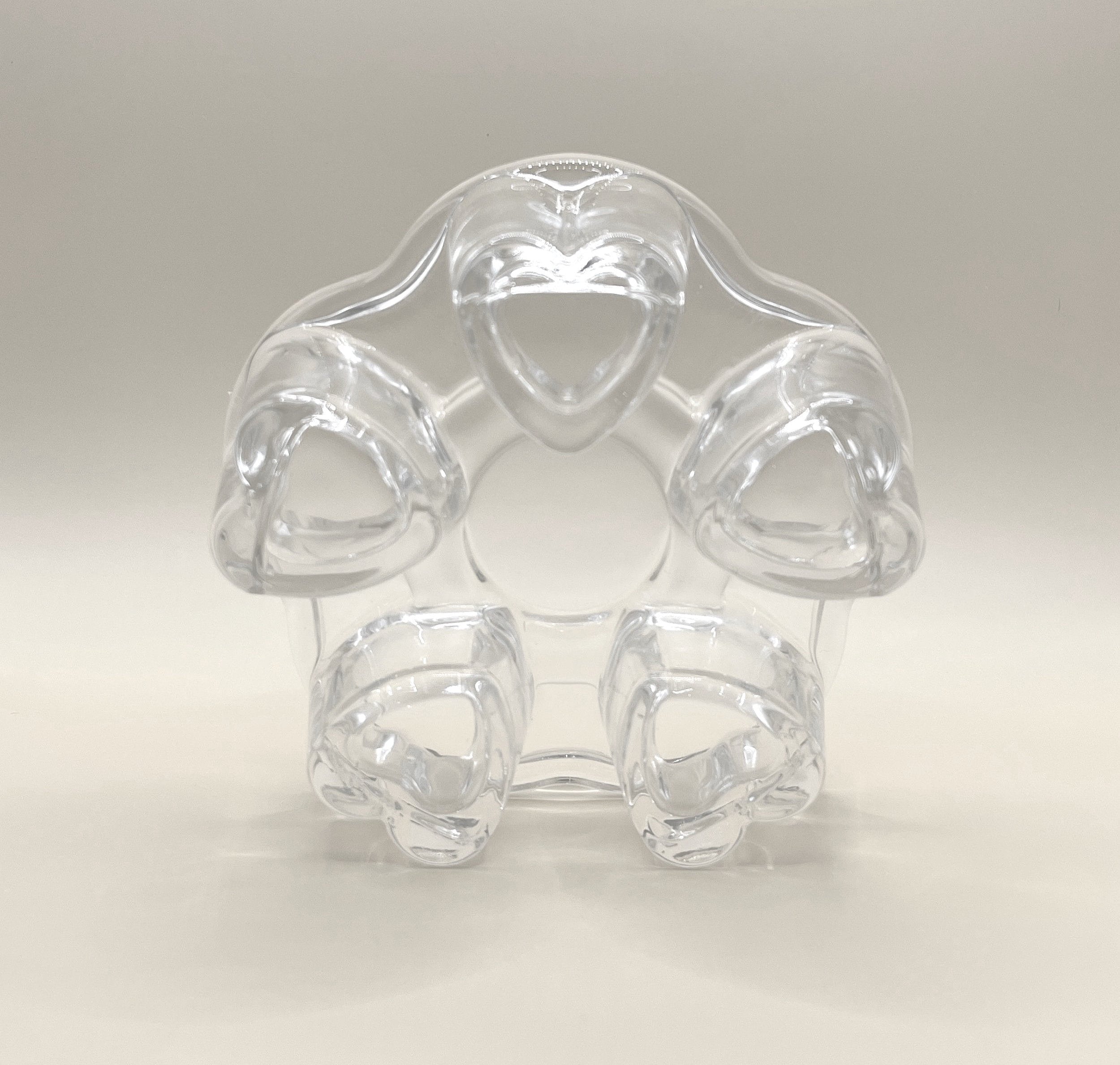 A clear, heart-shaped plastic ring, featuring five heart-shaped loops arranged in a circular pattern around a central opening, is reminiscent of the charm of the CozyGlow Tea Warmer by My Store. The object is set against a plain, light background.