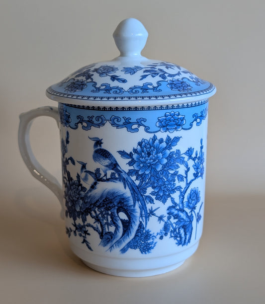 Blue and white ceramic mug with floral and bird design on a beige background