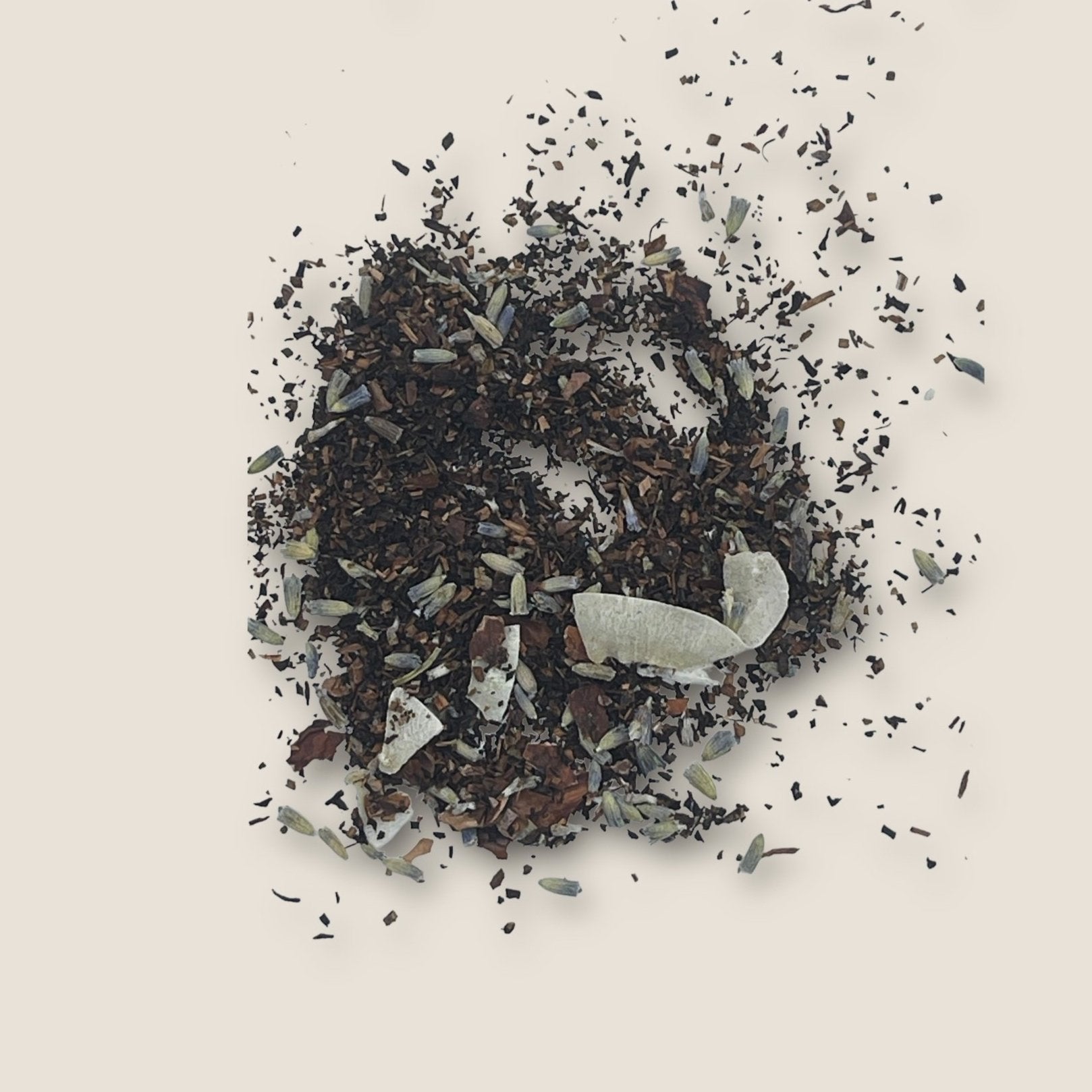 A scattered pile of Bear's Hug Tea from My Store on a light background. The mix includes small, dark tea leaves, dried flower petals, and white, thin slices of dried fruit or other botanical ingredients. Perfect for relaxation and promoting digestive health with its natural blend of antioxidants.