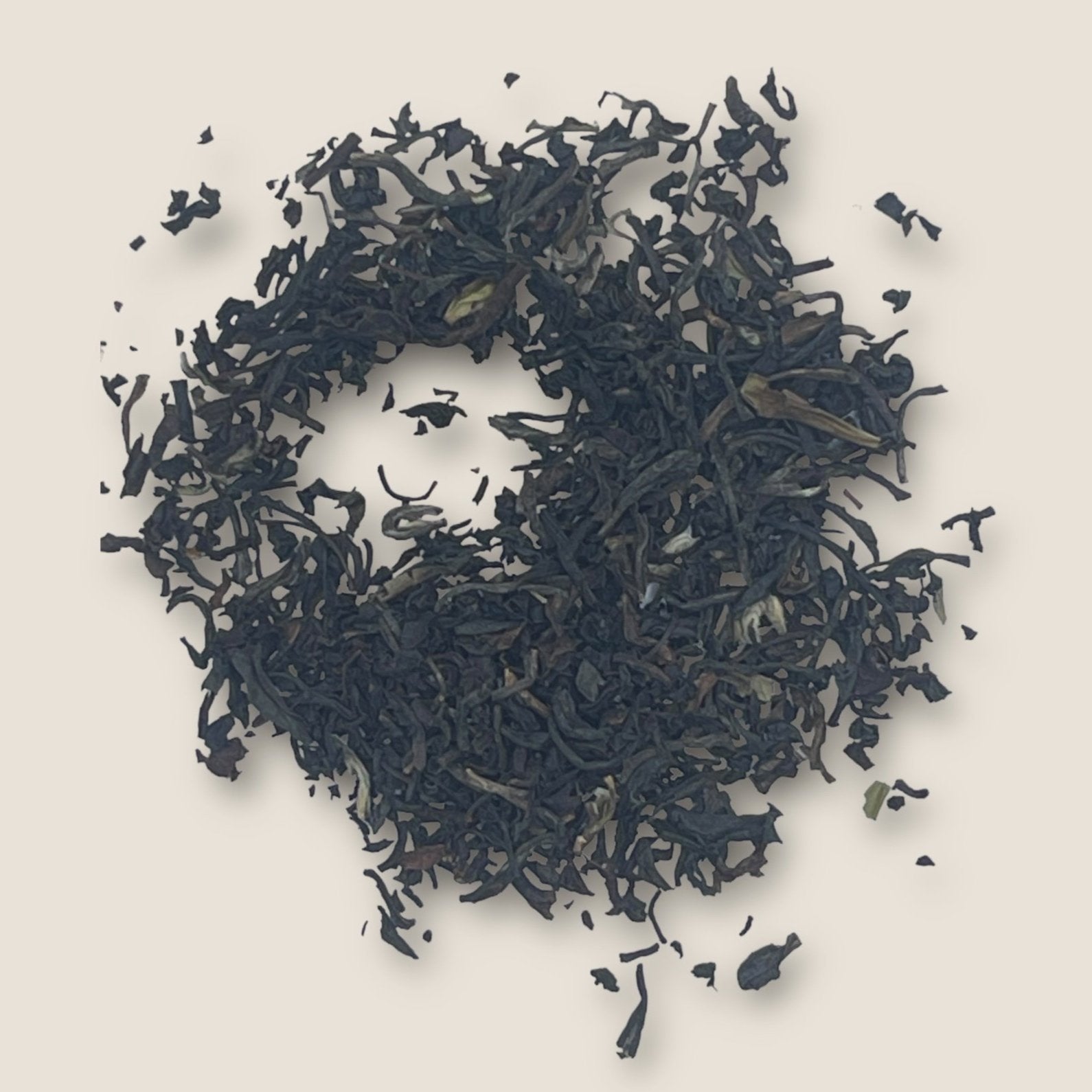 A circular arrangement of My Store's English Breakfast loose black tea leaves is displayed on a beige background. The tea leaves, rich in antioxidants for heart health, vary in size and form a textured, uneven pattern. Some smaller fragments are scattered around the main cluster.