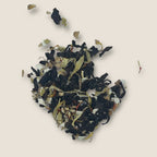 A heap of Golden Oolong loose-leaf tea from My Store, featuring a blend of black, white, and green leaves mingled with Oolong tea and various dried flowers and herbs, all scattered on a light beige background.
