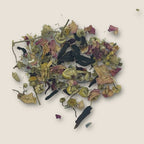 A pile of Lovers Hypnotised from My Store, known for its antioxidants and sleep aid properties, consists of dried chamomile flowers, green stems, and scattered pink rose petals against a neutral background. The ingredients are various shades of green, yellow, and pink.