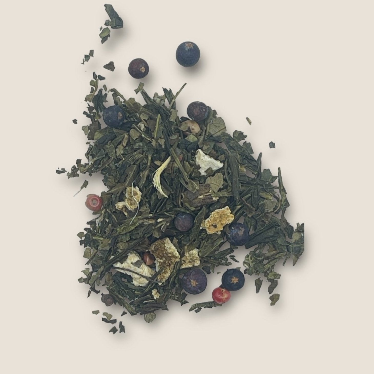 A mix of loose leaf tea from My Store's Gin 'n' Tonic blend featuring Sencha green tea leaves, pieces of dried citrus peel, and small round berries scattered on a light beige background. The ingredients are varied in color and texture, creating a visually appealing blend rich in antioxidants for added immune support.