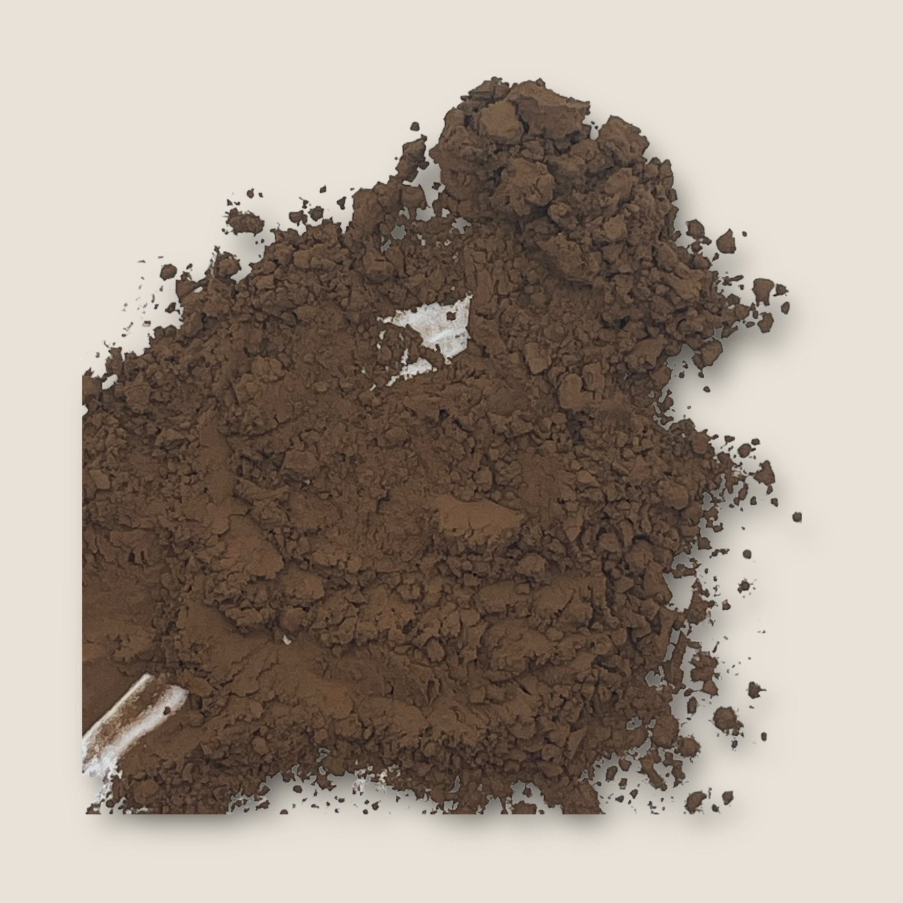A scattering of finely ground brown powder, identified as My Store's Cocoa Powder, is spread unevenly against a plain cream background. Some clumps are larger, while others are more powdery, giving the texture a varied, earthy appearance with hints of antioxidants known to boost cognitive function.
