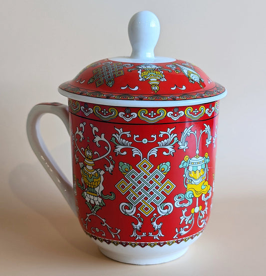 Red ceramic mug with intricate patterns and a white lid on a beige background