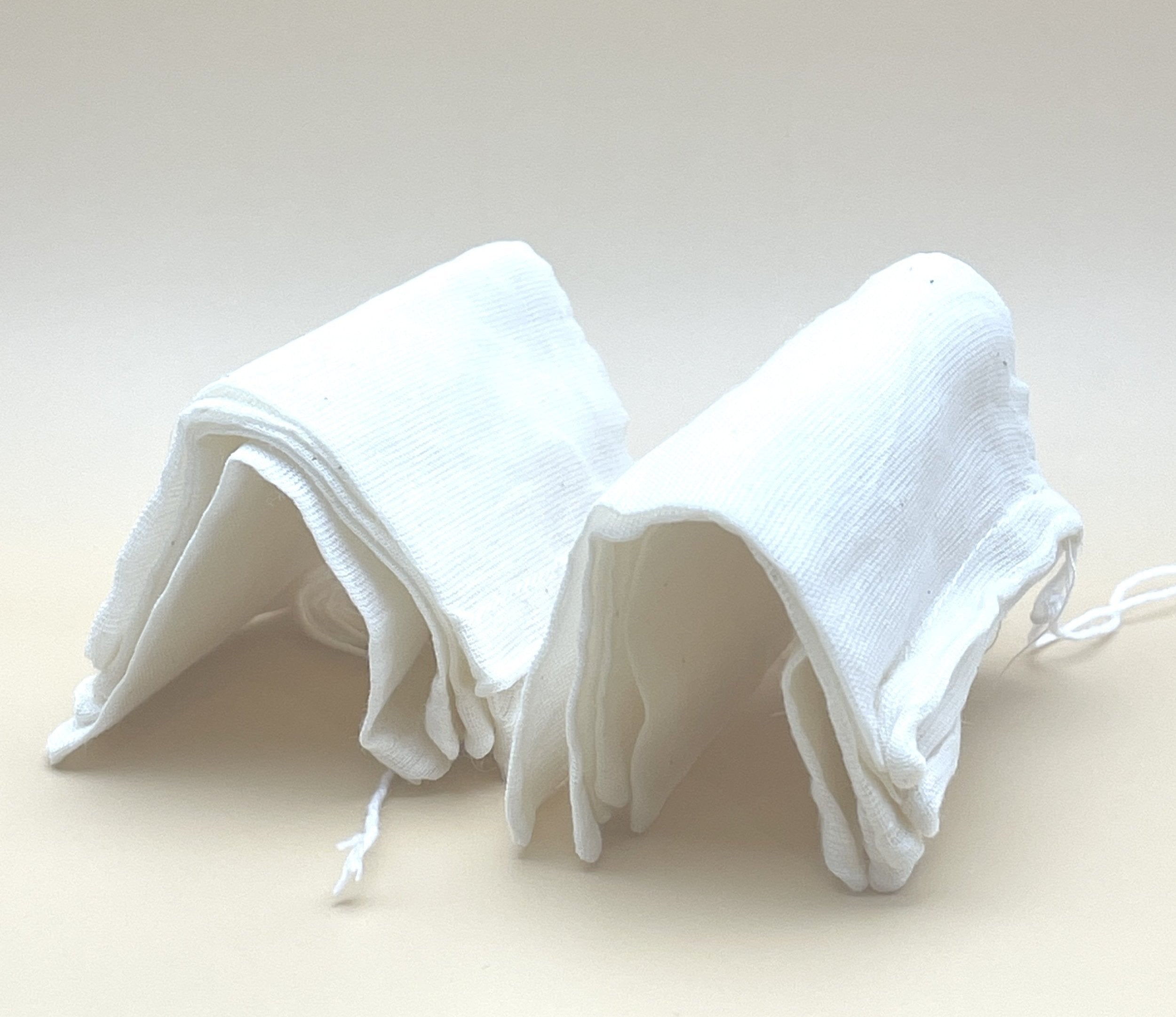 A stack of folded My Store's EcoPure Cotton Tea Bags, crafted from unbleached cotton, is arranged in two neat piles on a plain, light-colored surface. The tea bags' soft texture and tidy folds are clearly visible.