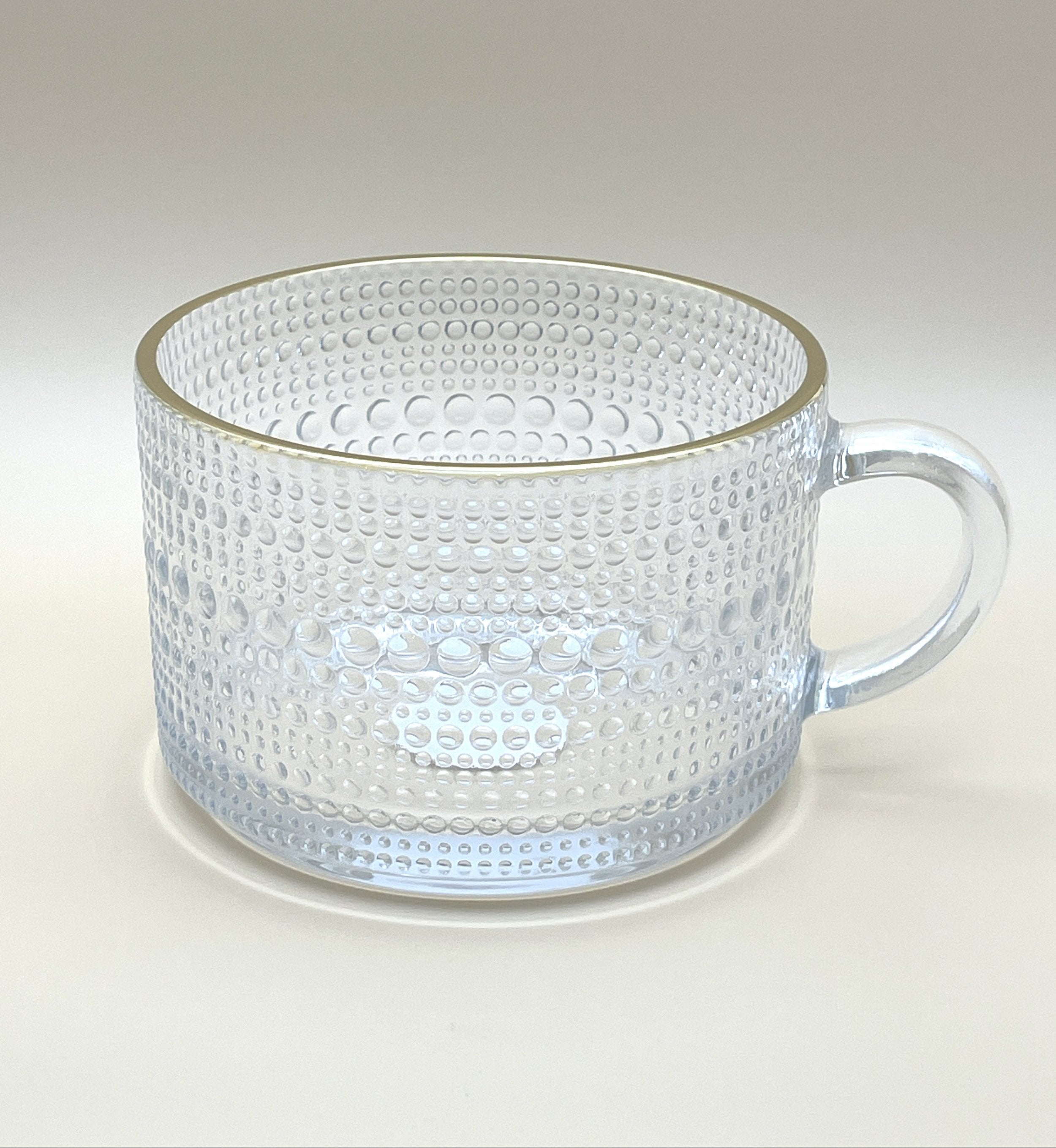 The 'Golden Aura Cup' from My Store is a clear glass mug adorned with a textured design of raised dots and features a handle on the right side. Crafted from high-quality soda glass, this kitchenware item sits empty against a plain, light background.